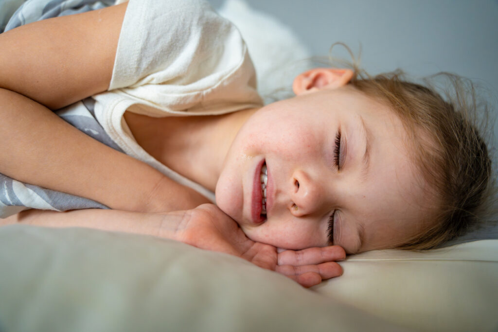 Child sleeping with gritted teeth, to illustrate what to do if your kid is grinding their teeth