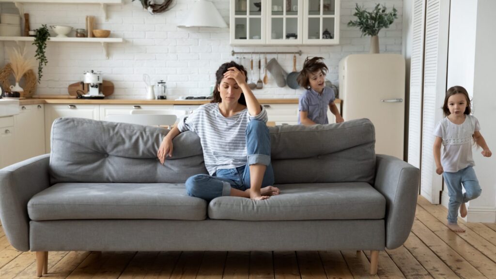 Exhausted parent with kids running around, to illustrate gentle parenting burnout