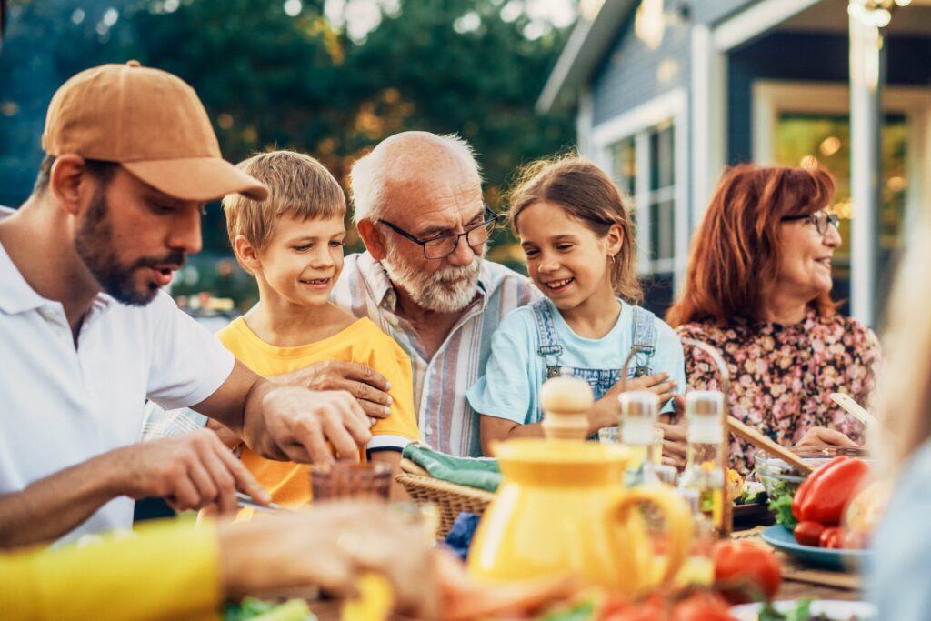 An involved grandparent sits at the table with their grandkids looking happy