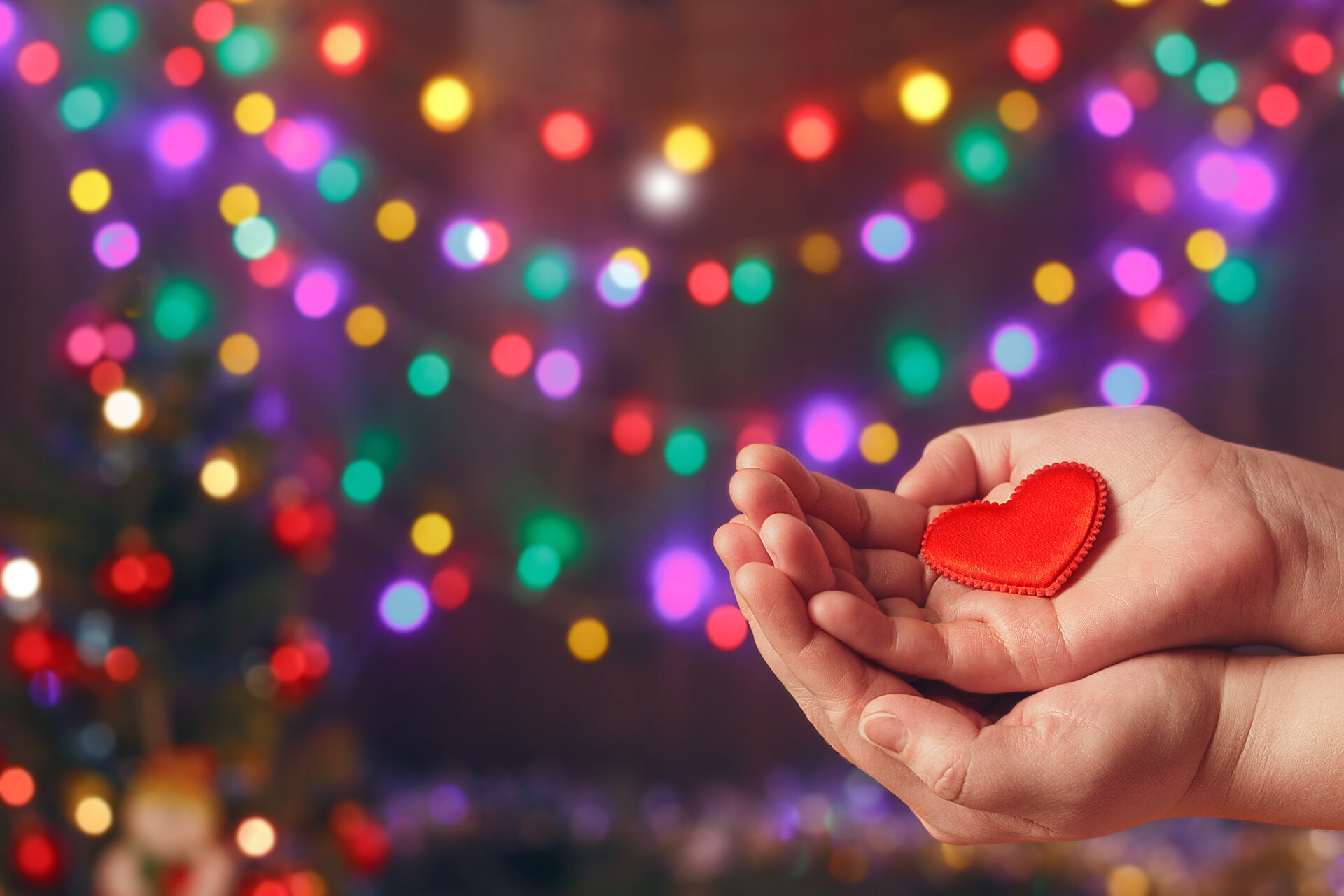 Small toy heart in hands, on a Christmas light backdrop, to illustrate how to reach out for help during the holidays