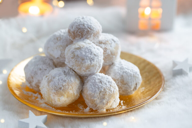 Snowball cookies covered in powdered sugar and sitting on a gold plate