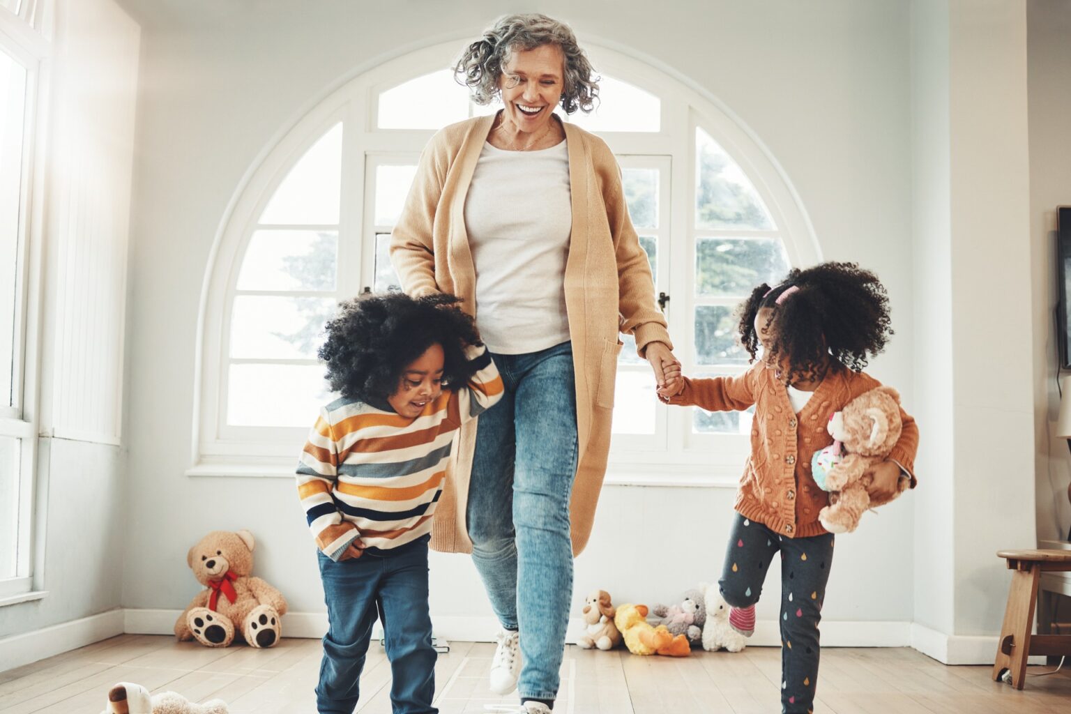 A grandmother holds the hands of her two grandchildren and they look like they are moving quickly around in active play