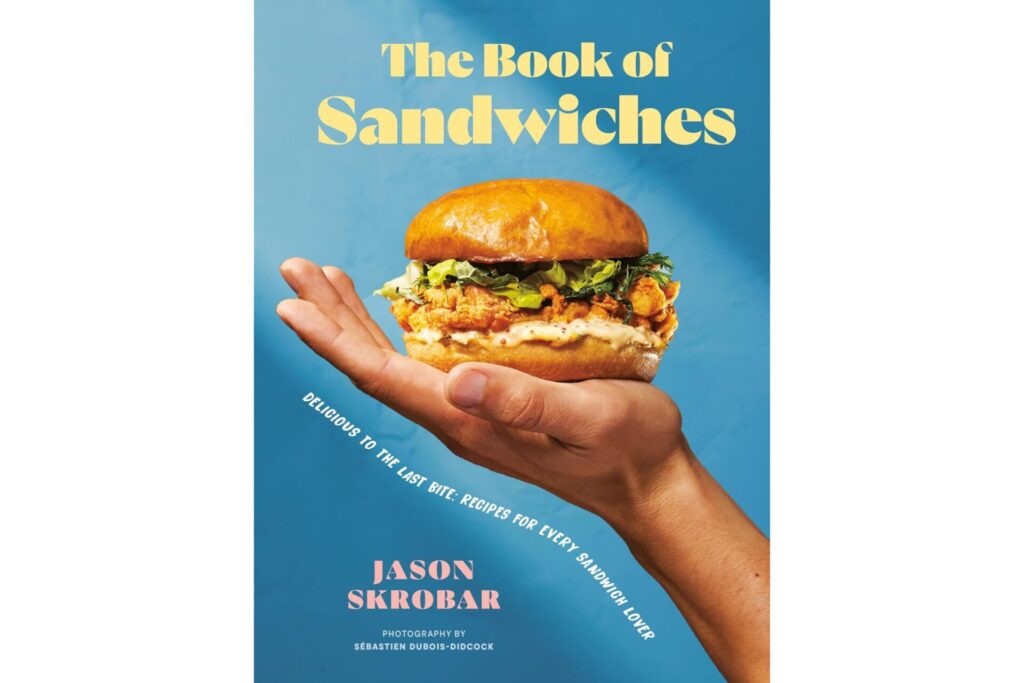 Cover of the book of sandwiches cookbook that has a hand holding up a tasty-looking burger