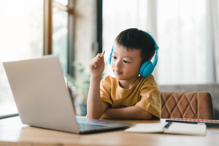 Asian child on computer with headphones to illustrate student tech