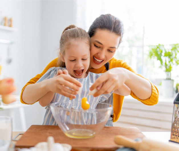Mother and daughter cracking an egg into a mixing bowl