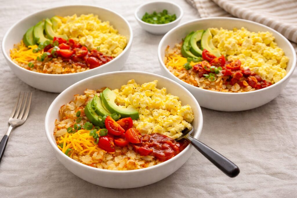 Scrambled eggs, hash bowns and toppings in white bowls