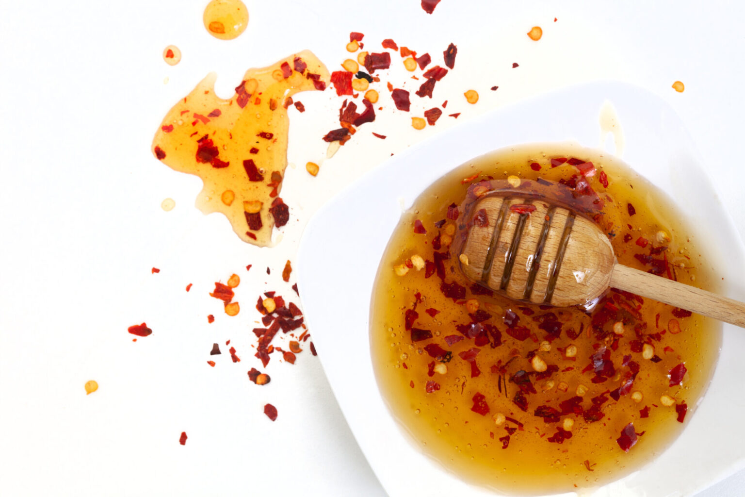 Homemade hot honey in a white bowl, with a honey dipper