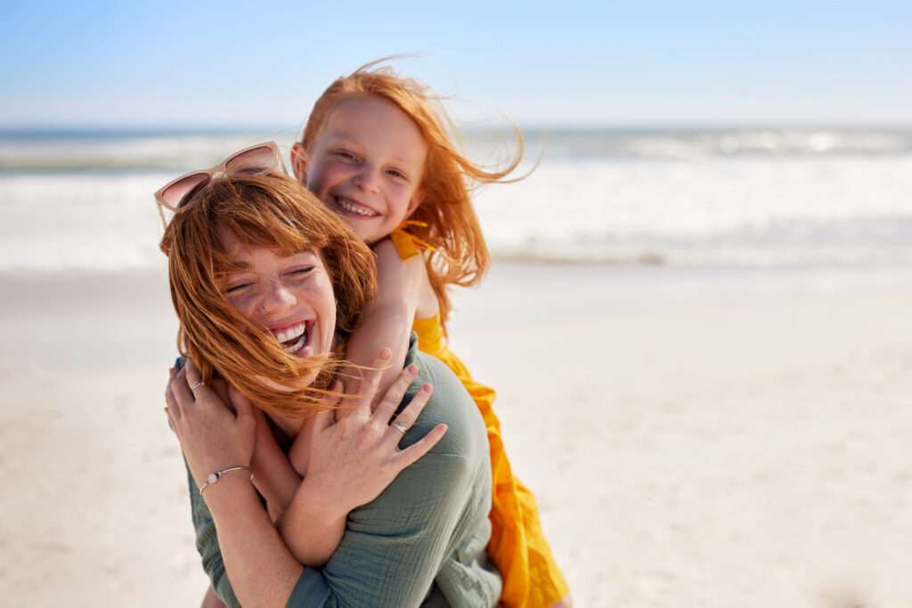 A red-headed mom and daughter playing on the beach during no-buy summer
