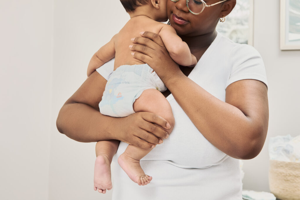 Mom holding baby wearing Pampers Swaddlers diaper, for newborn diaper-changing hacks