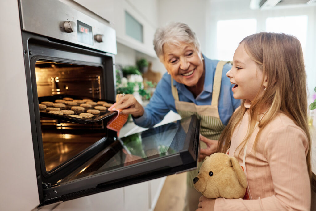 Grandparent and child taking a tray of cookies out of the oven. 