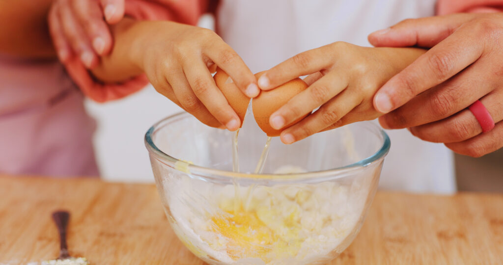hands of child and grandparent cracking an egg into a bowl