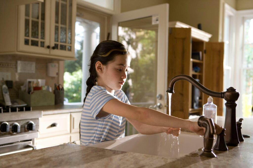 Child washing dishes for practical life skills to learn before age 18